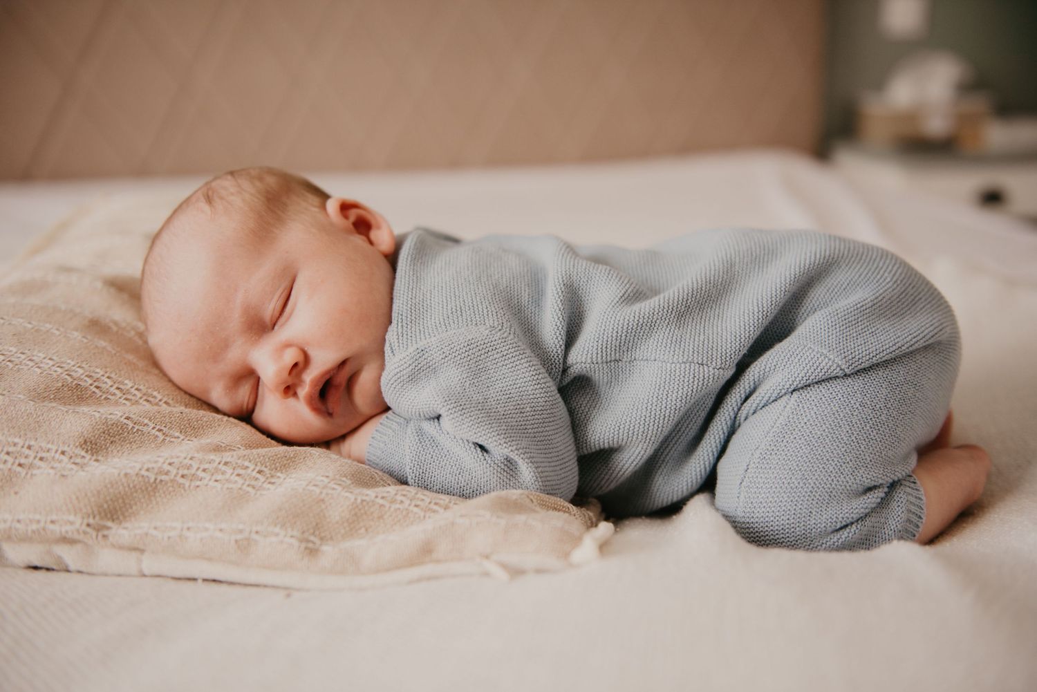 Newborn baby wearing cozy gray outfit resting peacefully on beige bedding.