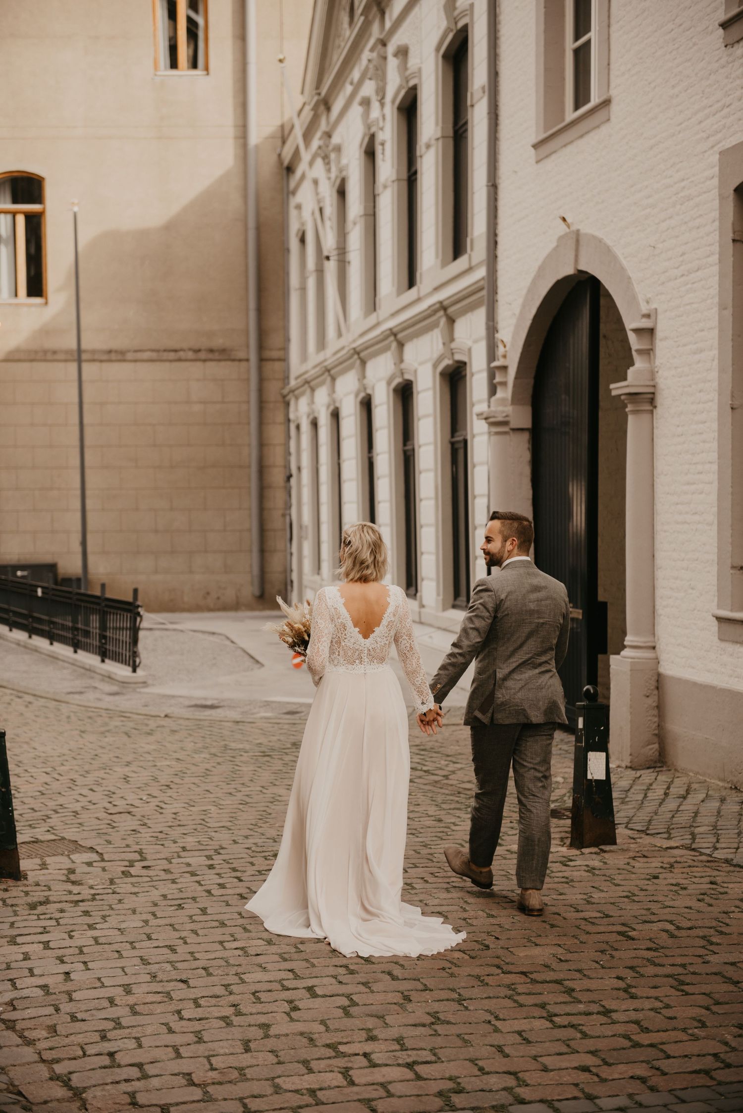 Couple walking along cobblestone street beside white historic building.