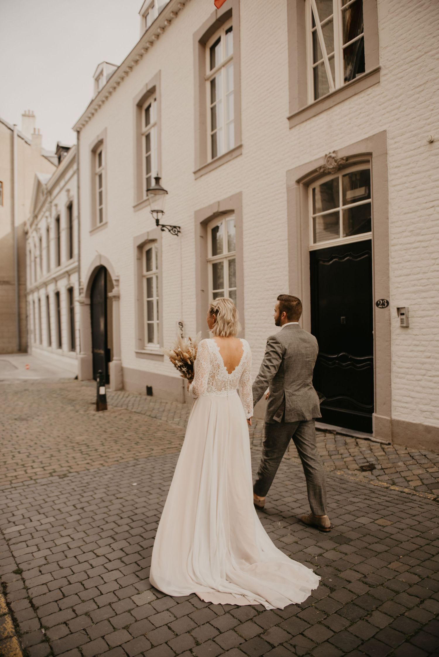 Wedding couple walking through European cobblestone street with white buildings.