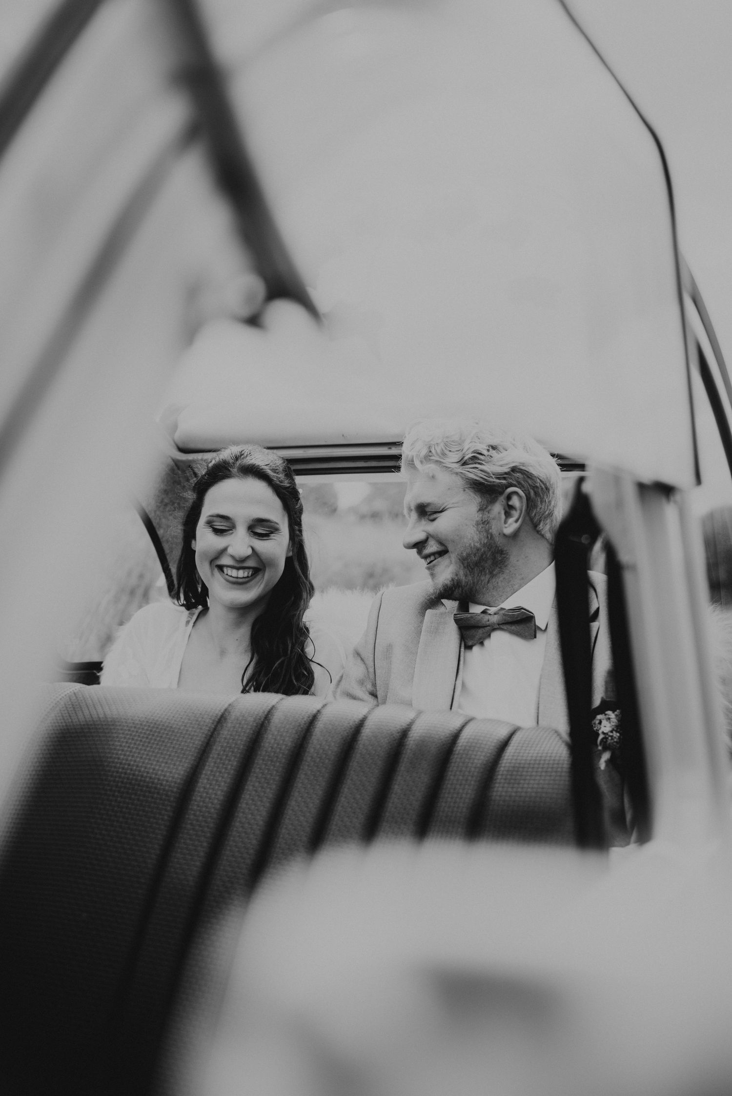Black and white candid moment captured through car window during wedding celebration.