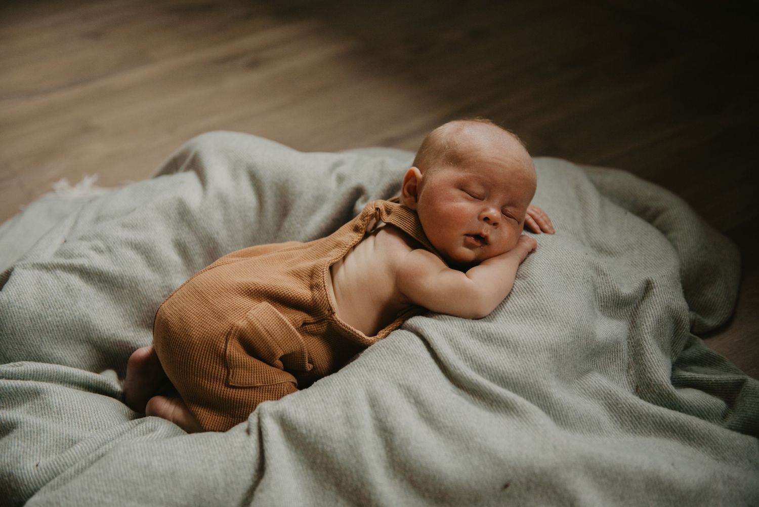 Sleeping newborn wrapped in soft blanket on grey bedding.