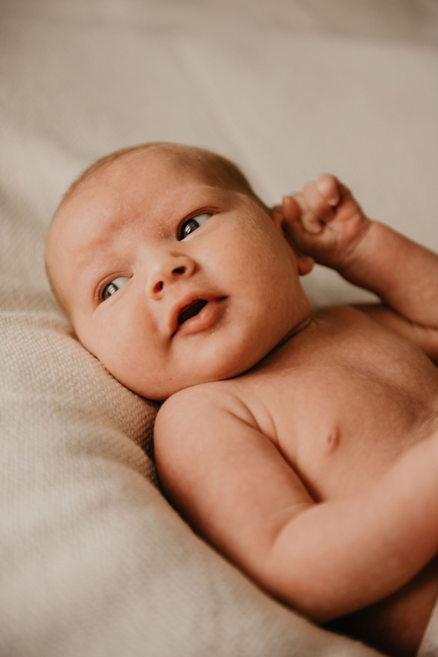 Close-up view of a newborn baby lying on soft beige fabric in natural light.
