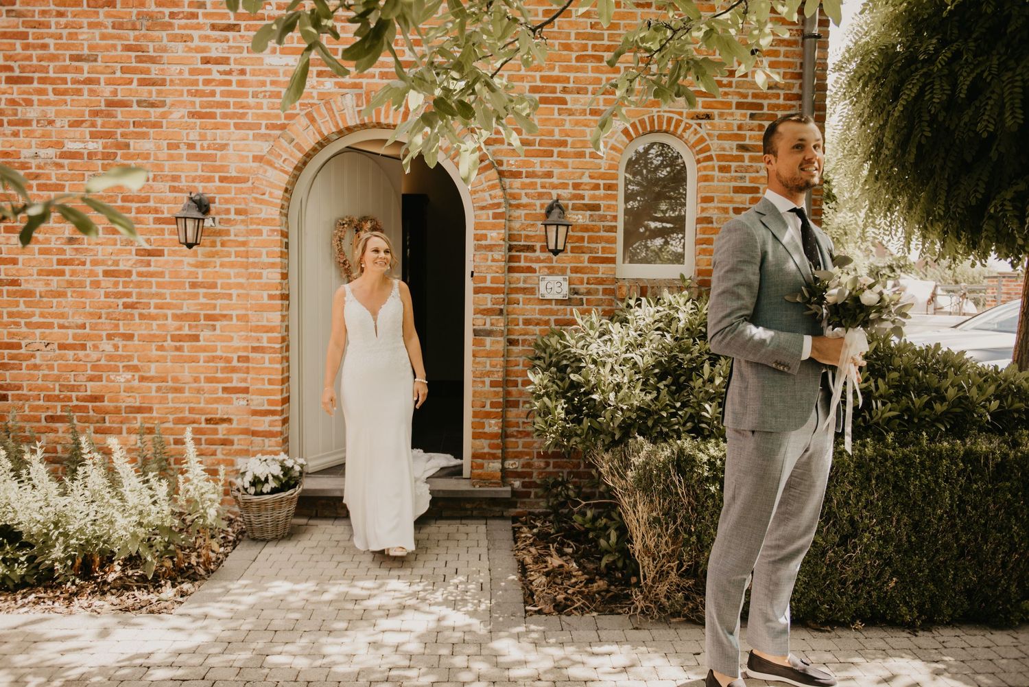 Wedding couple poses against rustic brick wall exterior.