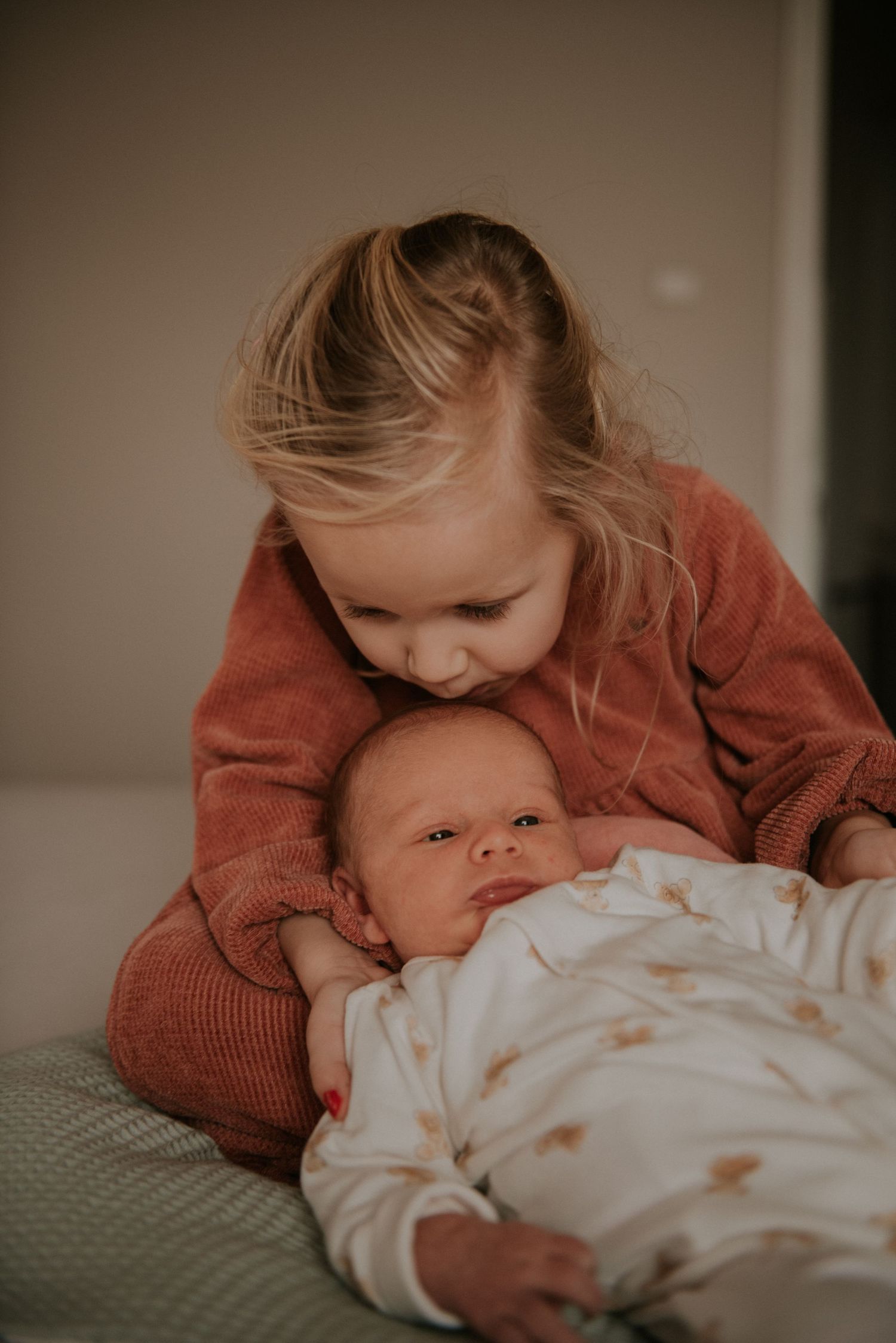 Sweet interaction between siblings on a cozy bed with neutral tones.