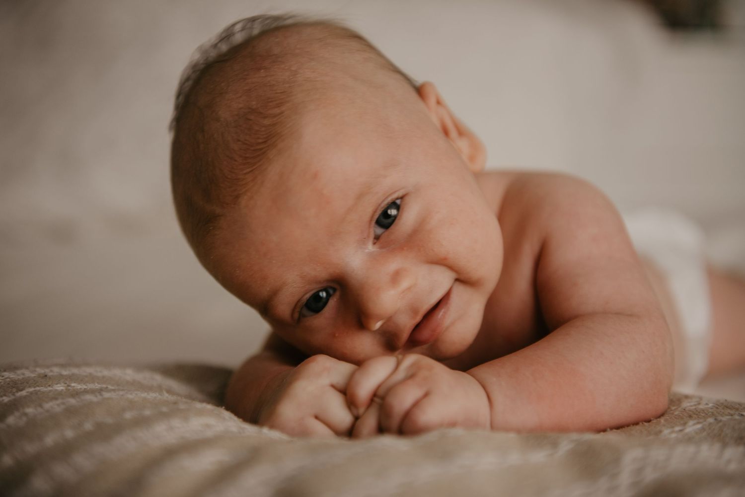 Side view of newborn baby resting on textured cream bedding.