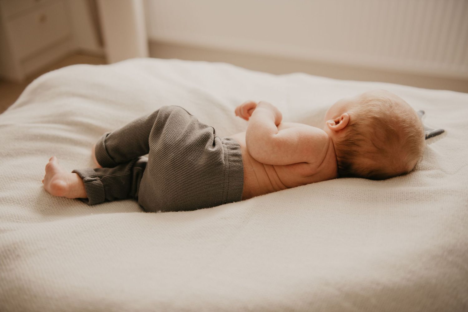 Sleeping newborn wrapped in soft fabric on neutral background.