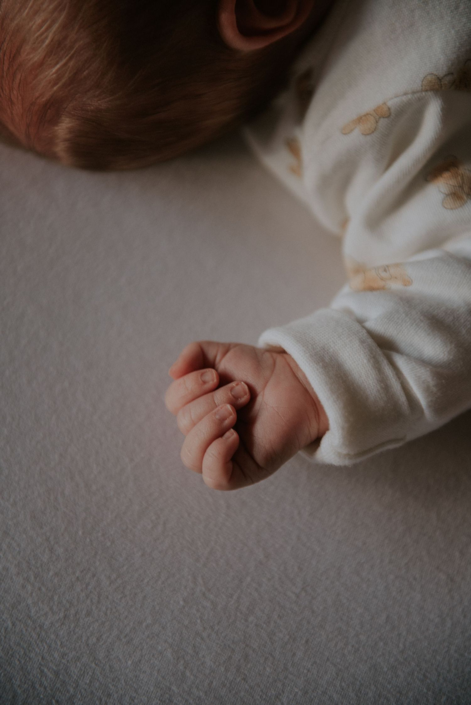 Newborn baby's tiny hands resting on white blanket in gentle lighting.