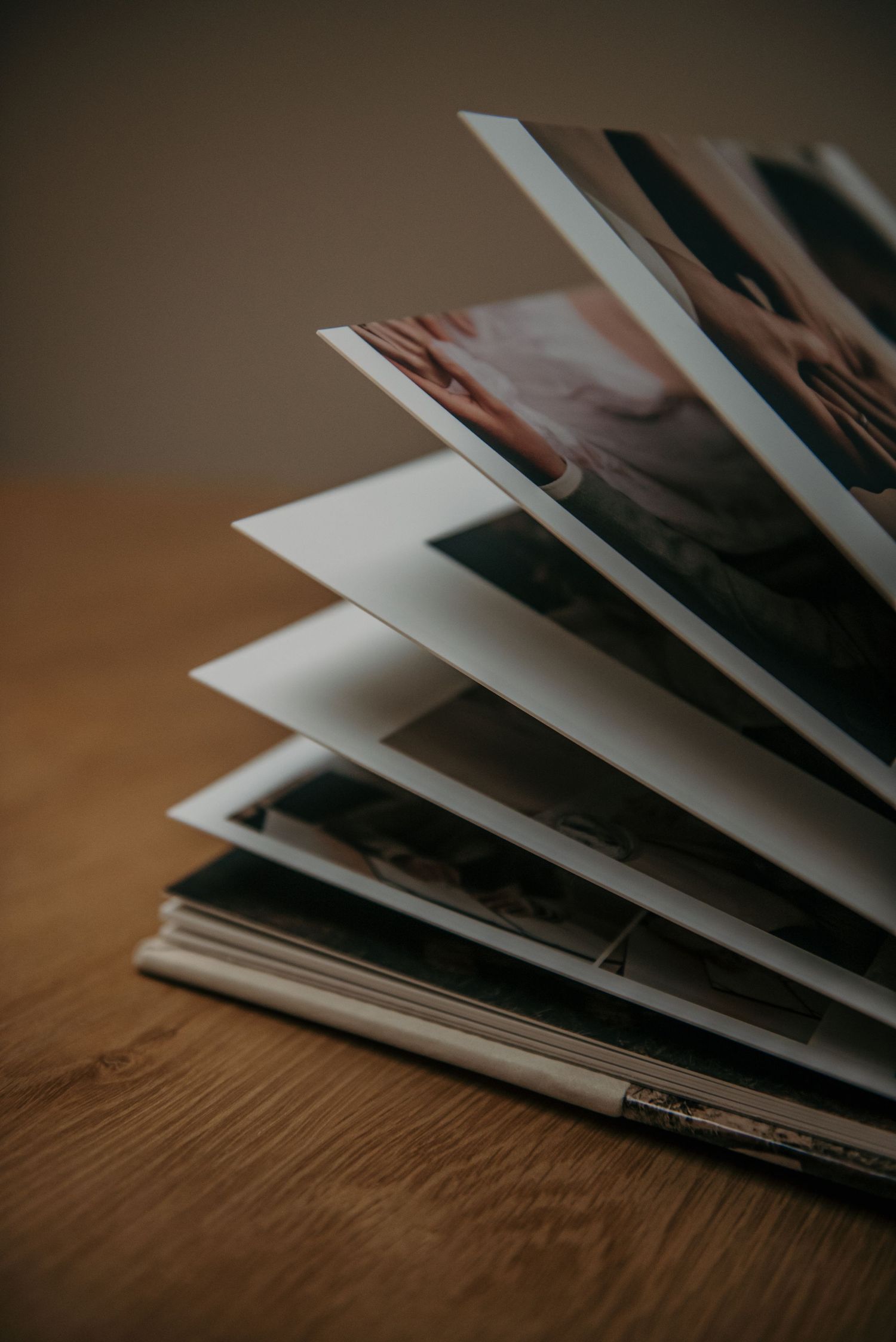 Stack of printed photographs spread out on wooden table surface.