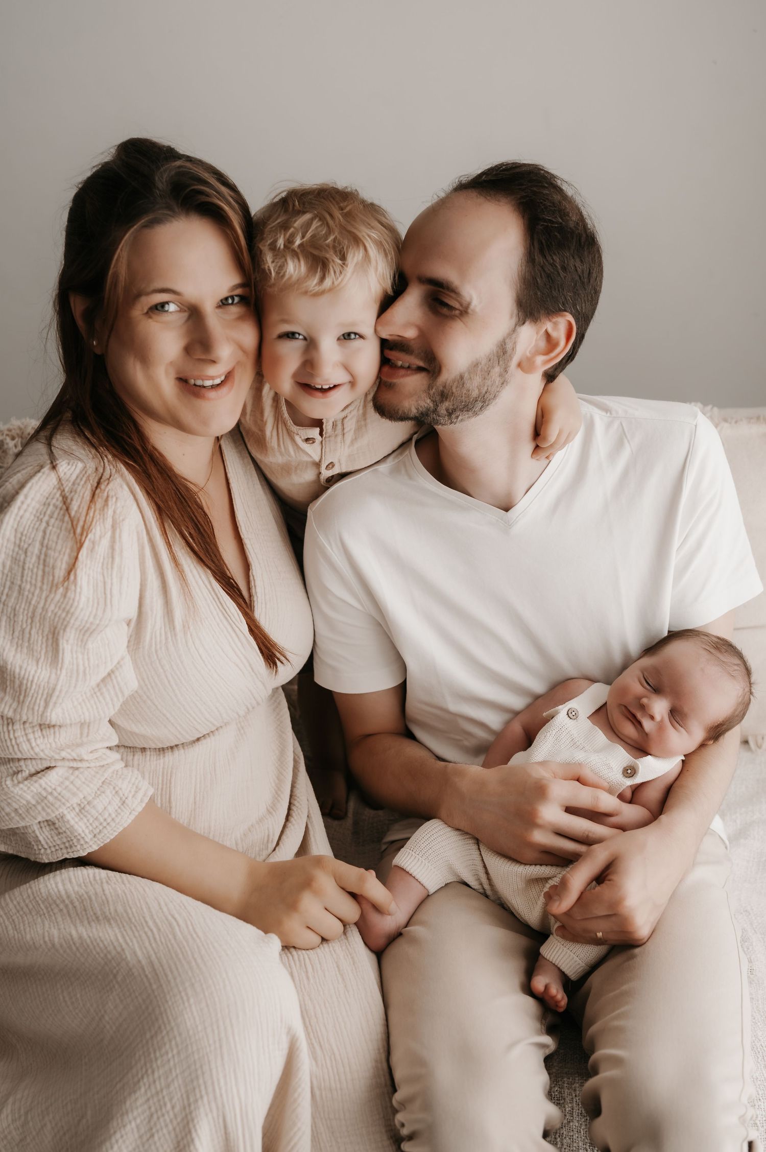 Intimate family photoshoot in neutral tones showing tender moments between parents and children on white backdrop.