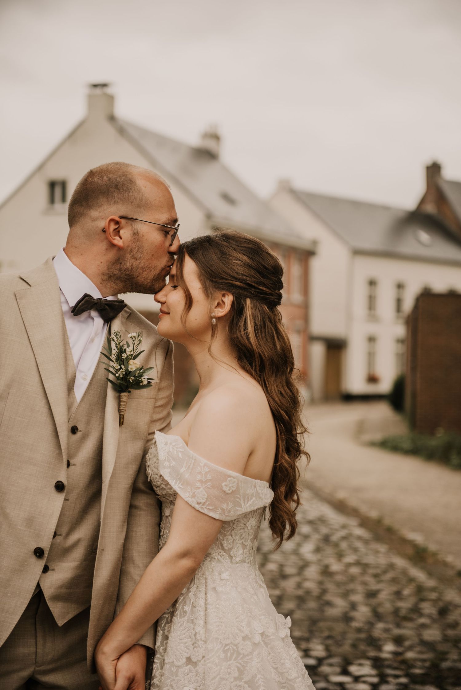 Romantic couple shares intimate moment on cobblestone street with rustic buildings in background.