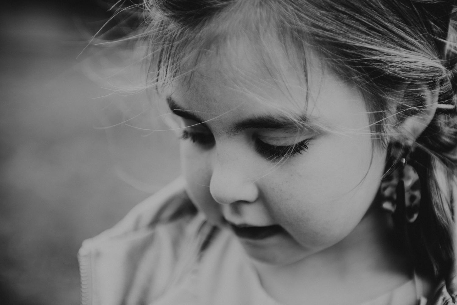 Black and white close-up portrait of a young child looking down with windswept hair.