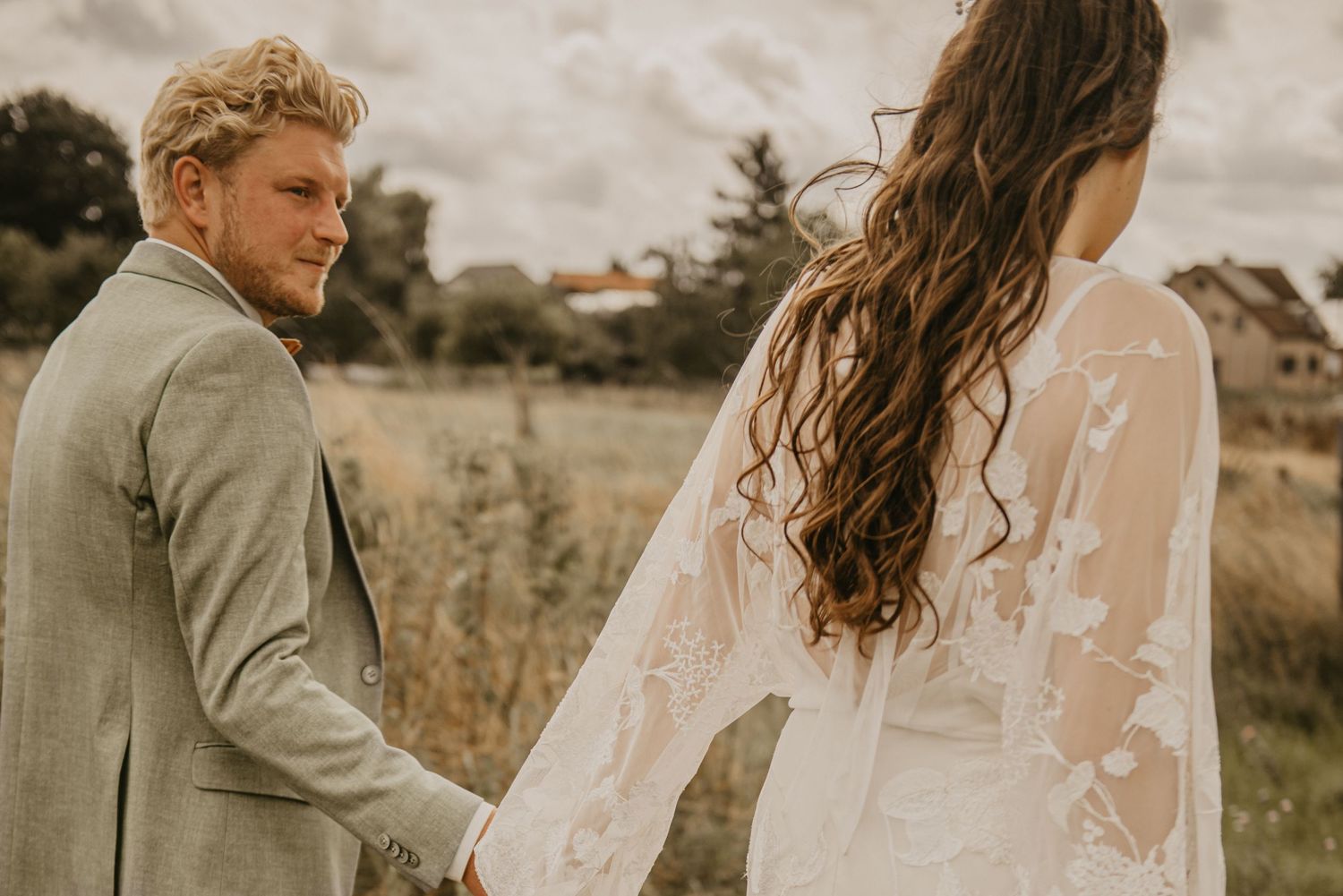 Romantic wedding couple poses together in a sunlit field.