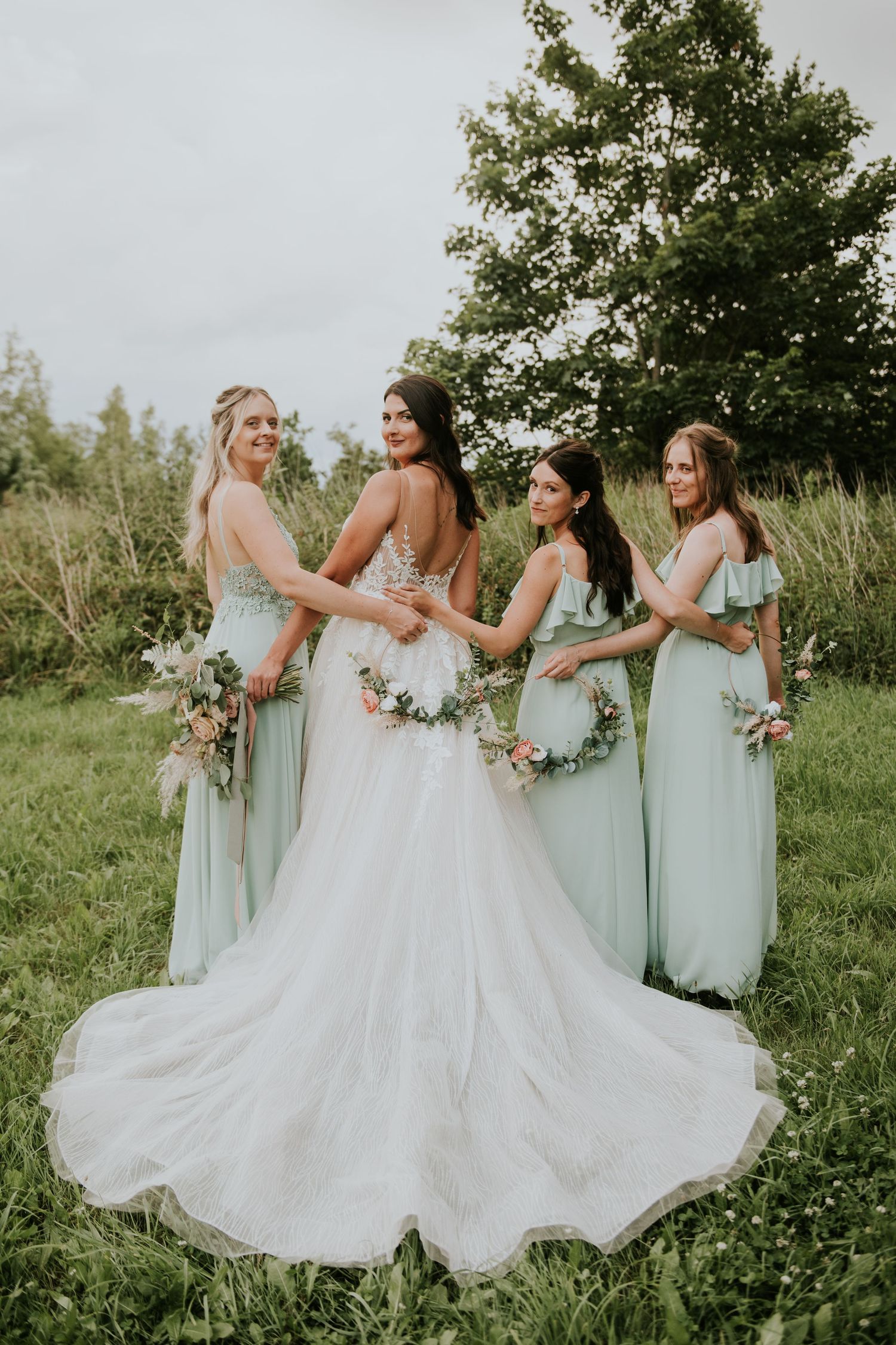 Bridesmaids in mint green dresses pose with bride in white gown against lush outdoor garden setting.