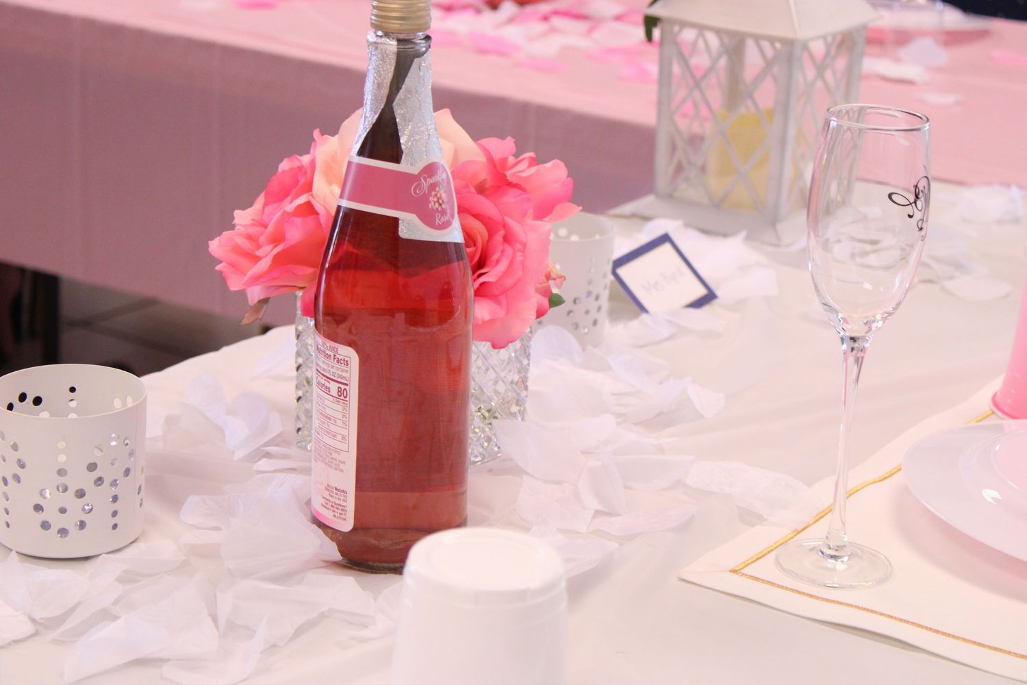 Pink party table setting with decorative bottle and tissue paper flowers.