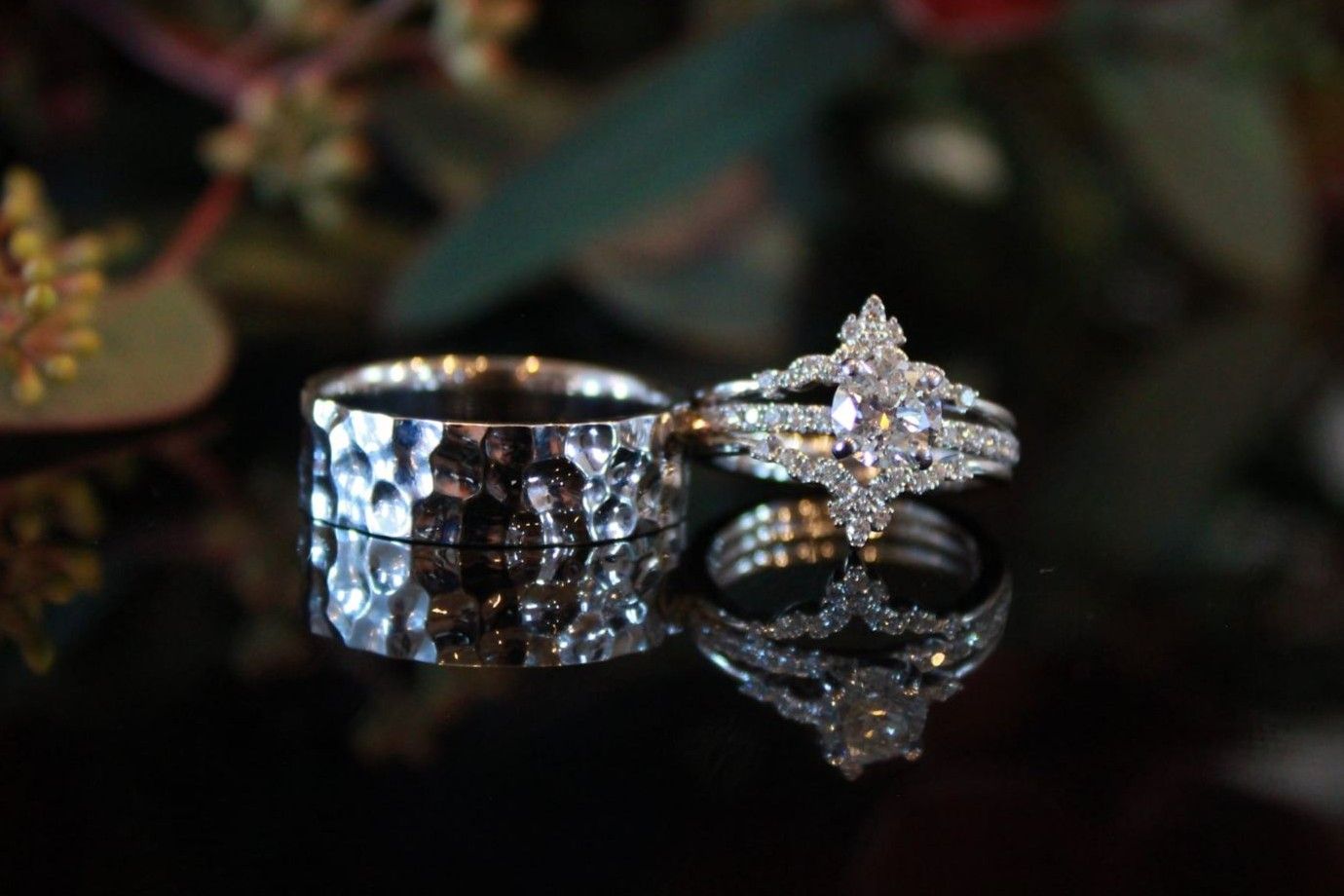 Detailed shot of wedding rings with textured metallic band and diamond setting on dark surface.