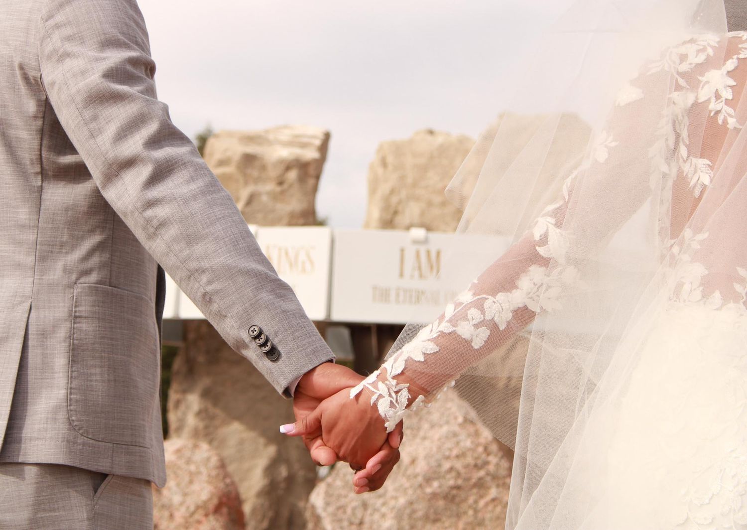 Wedding couple's hands tenderly touch while standing in formal attire outdoors.