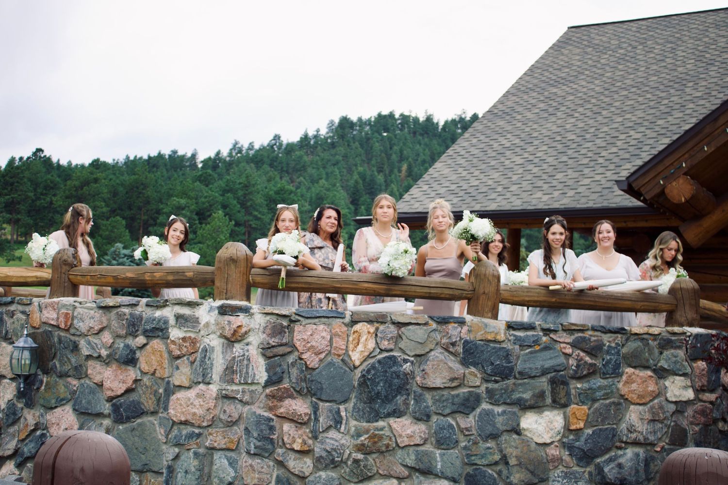 People gather around a scenic stone wall overlooking a mountain landscape during an outdoor celebration.