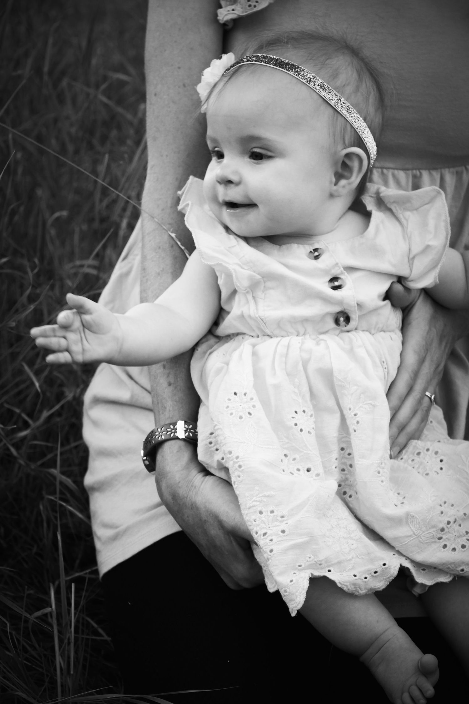 Black and white photo series showing a baby in white eyelet dress held at different angles against a dark background.