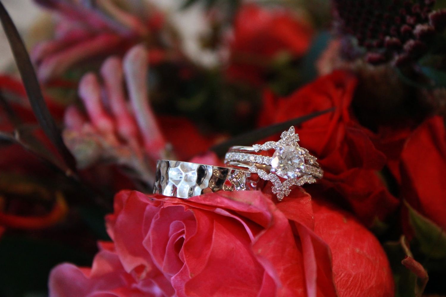 Diamond engagement rings displayed on a red rose in macro photography.
