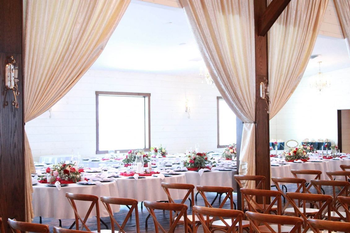 Elegant wedding venue with white drapes, wooden chairs and ocean view through windows.