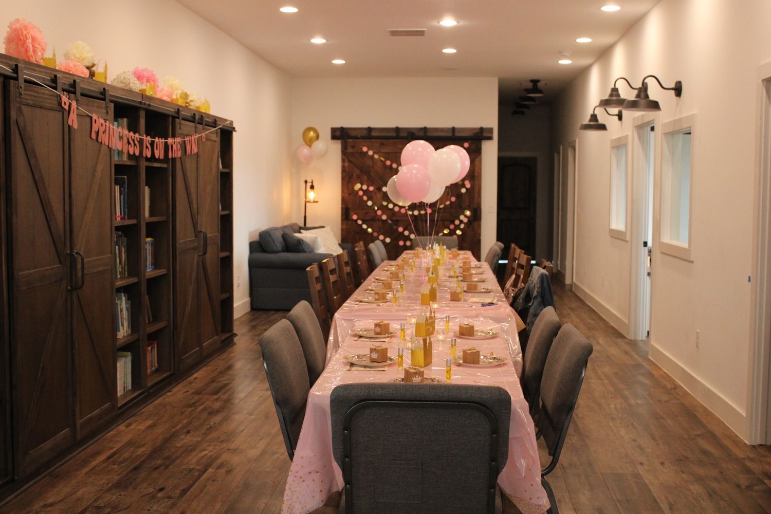 Long dining table with pink decor and barn door storage in modern event space.