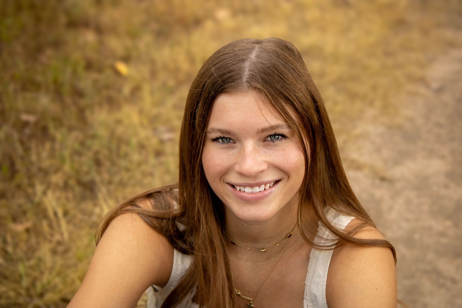 Young woman wearing a casual grey tank top poses outdoors with natural lighting and warm autumn colors in background.
