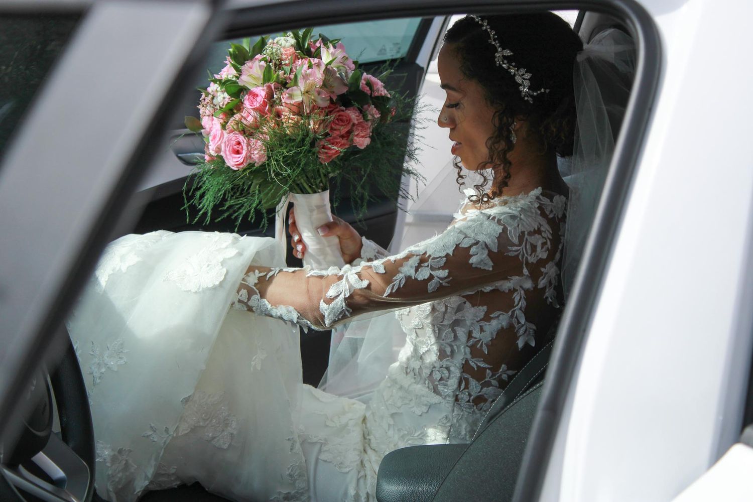 Person in a lace wedding dress sitting in a car with pink roses.