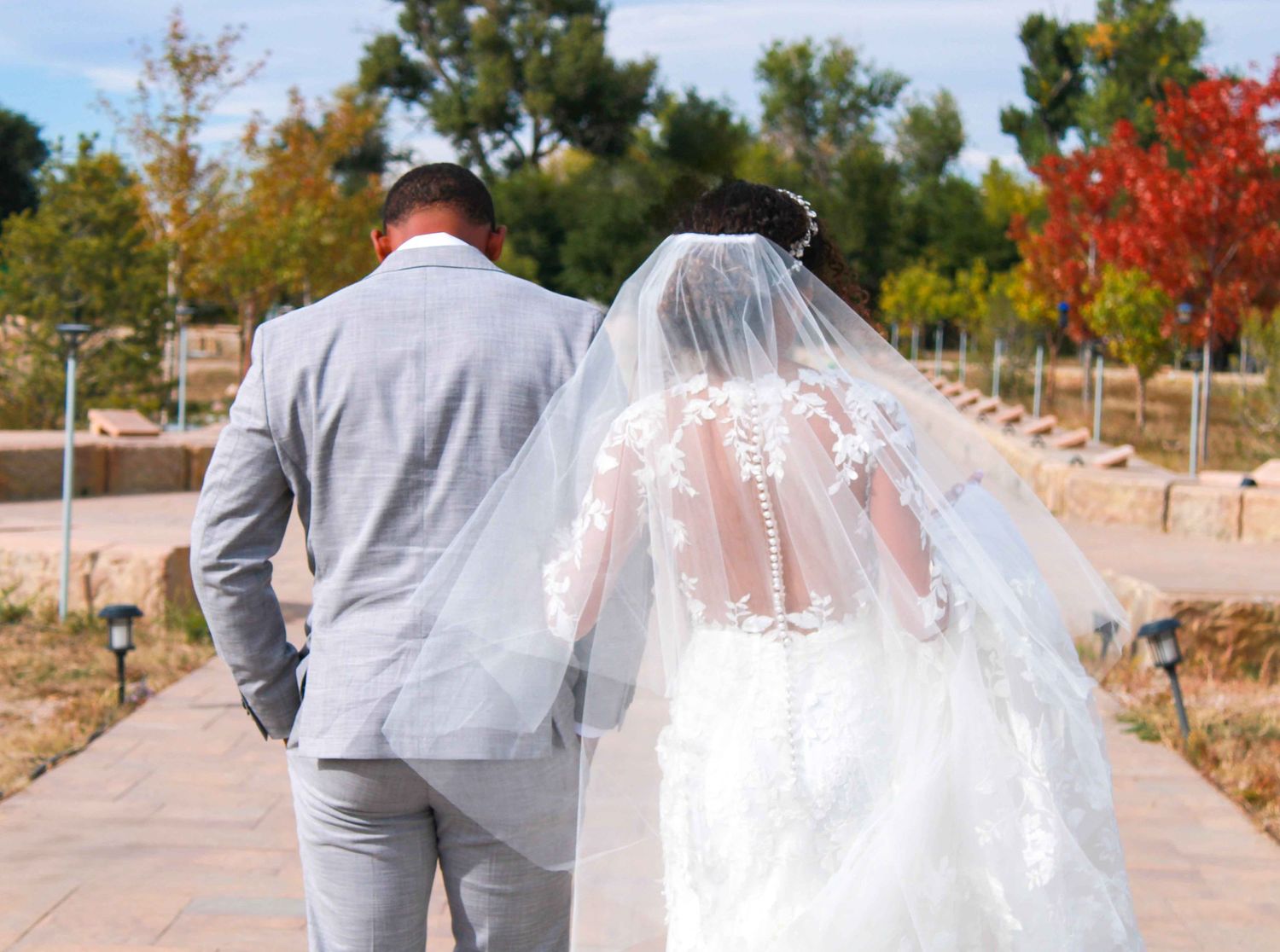 Couple in wedding attire walking down a pathway lined with autumn trees.