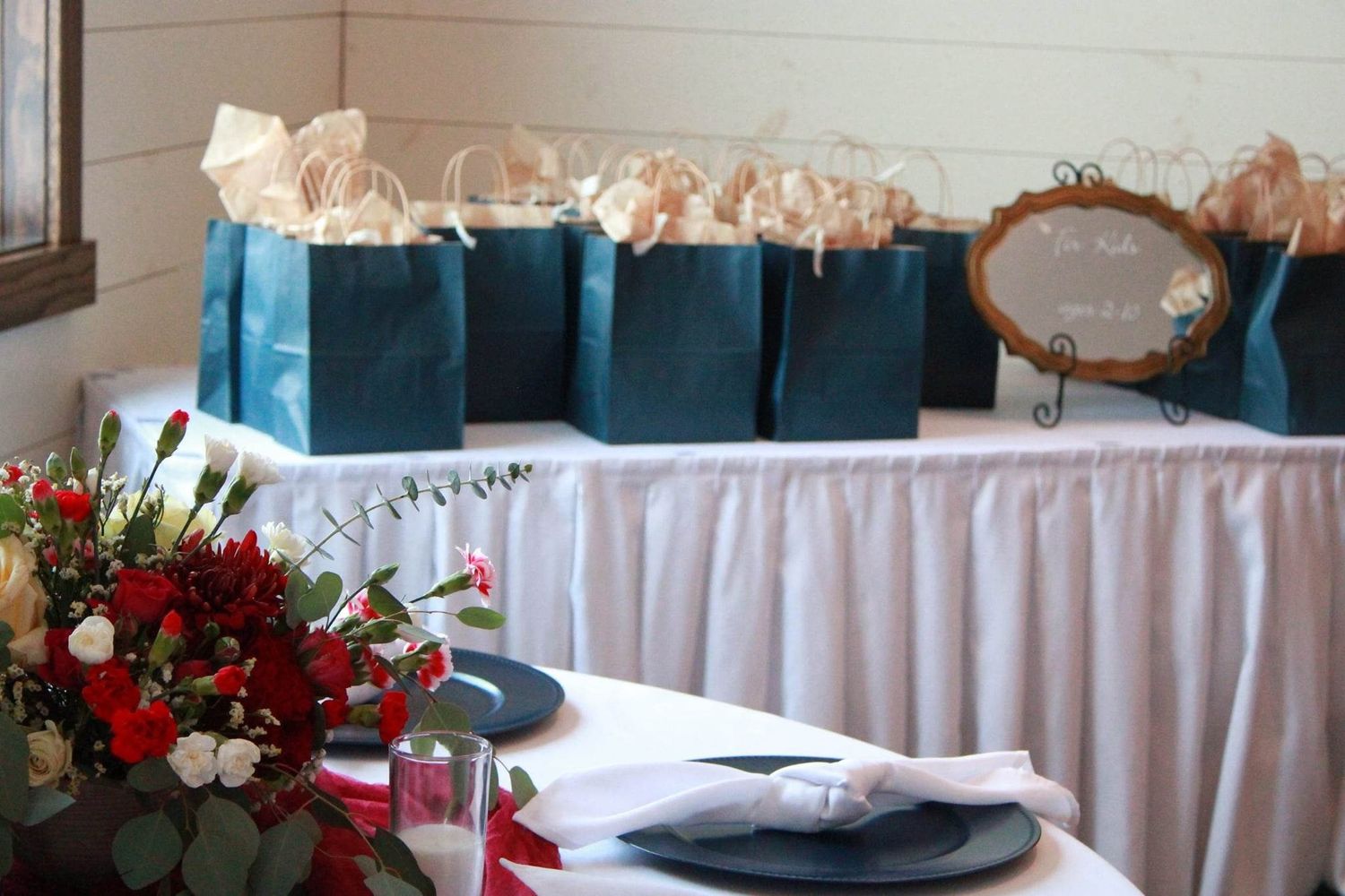 Wedding reception table decorated with teal gift bags and white linens.