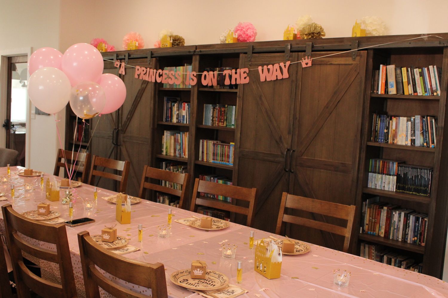 Party room decorated with pink balloons and rustic bookshelf wall.