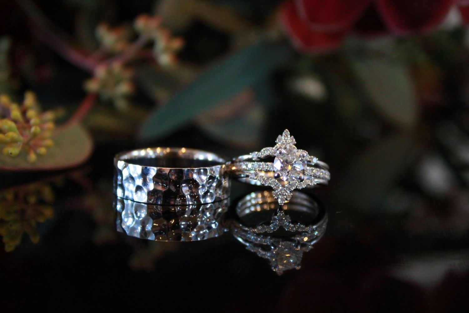 Close-up of elegant wedding rings with textured band and diamond engagement ring on dark reflective surface.