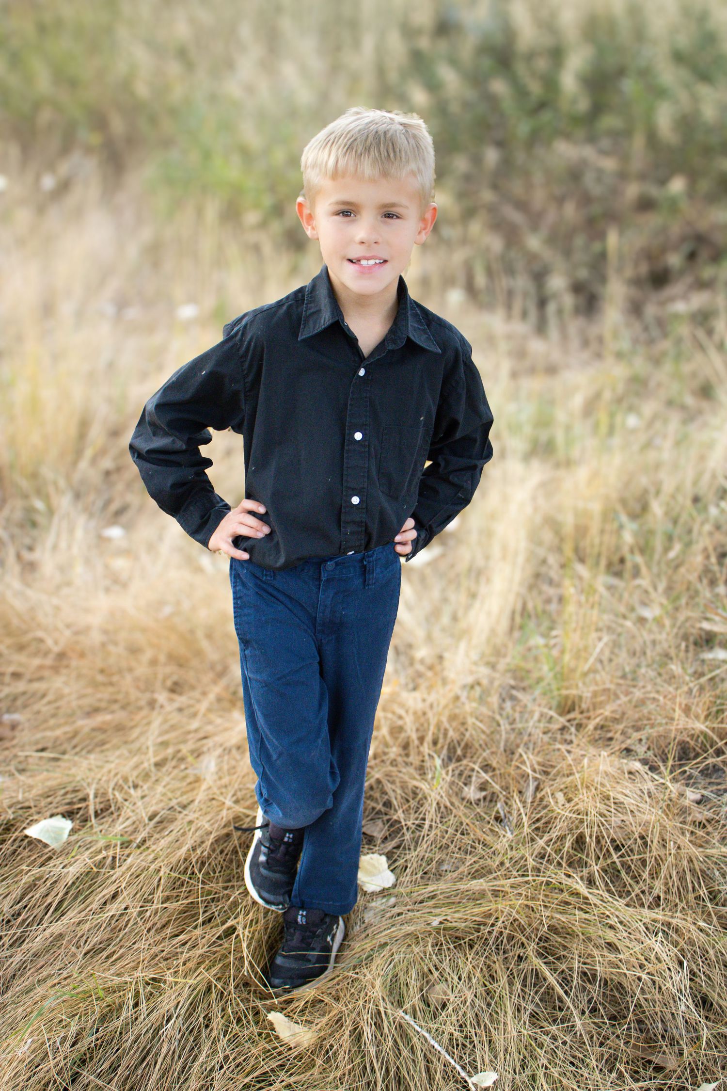 A child stands in tall grass wearing a black button-down shirt and blue jeans.