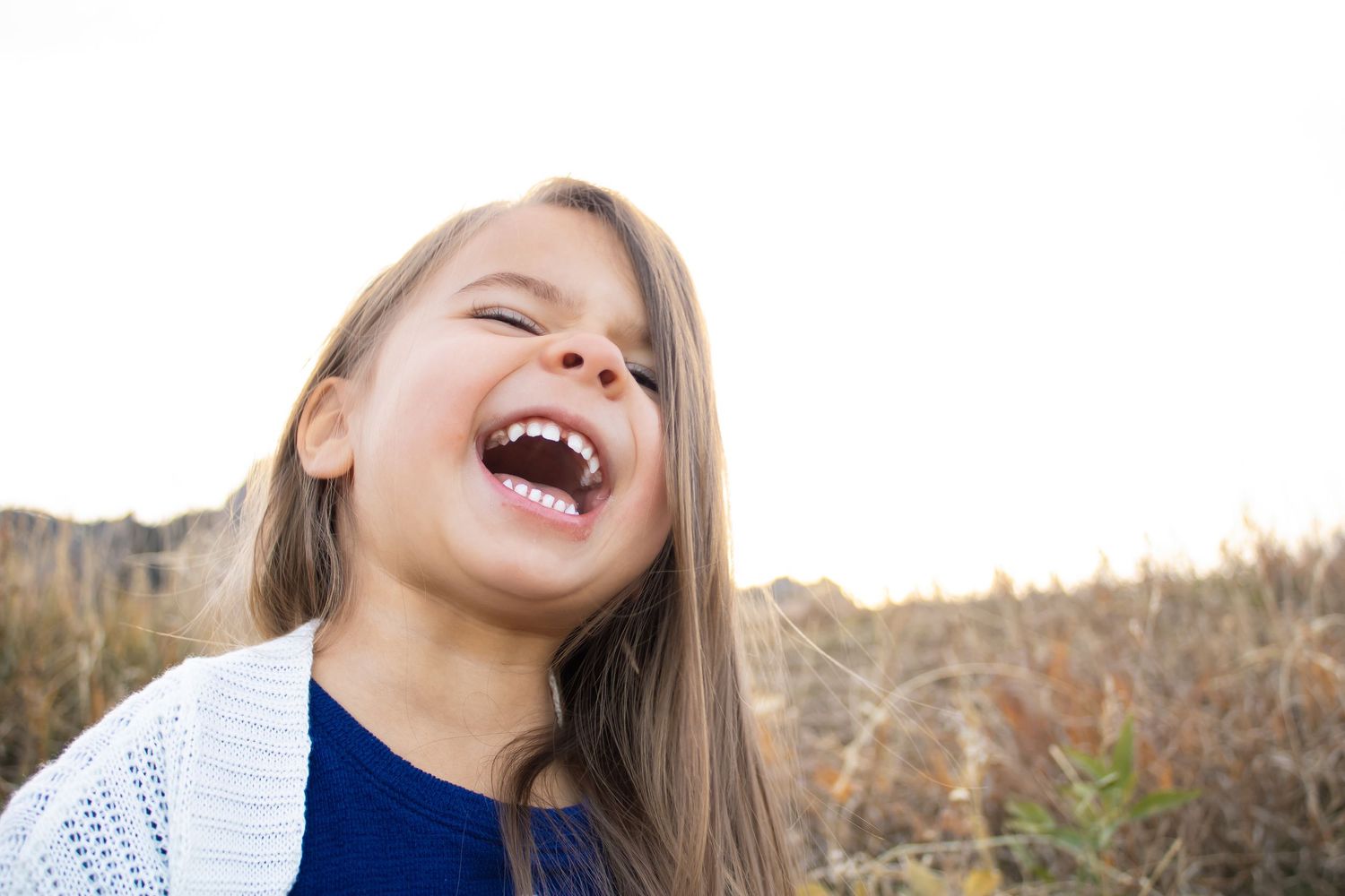 A joyful child with long hair laughs outdoors during golden hour in autumn.