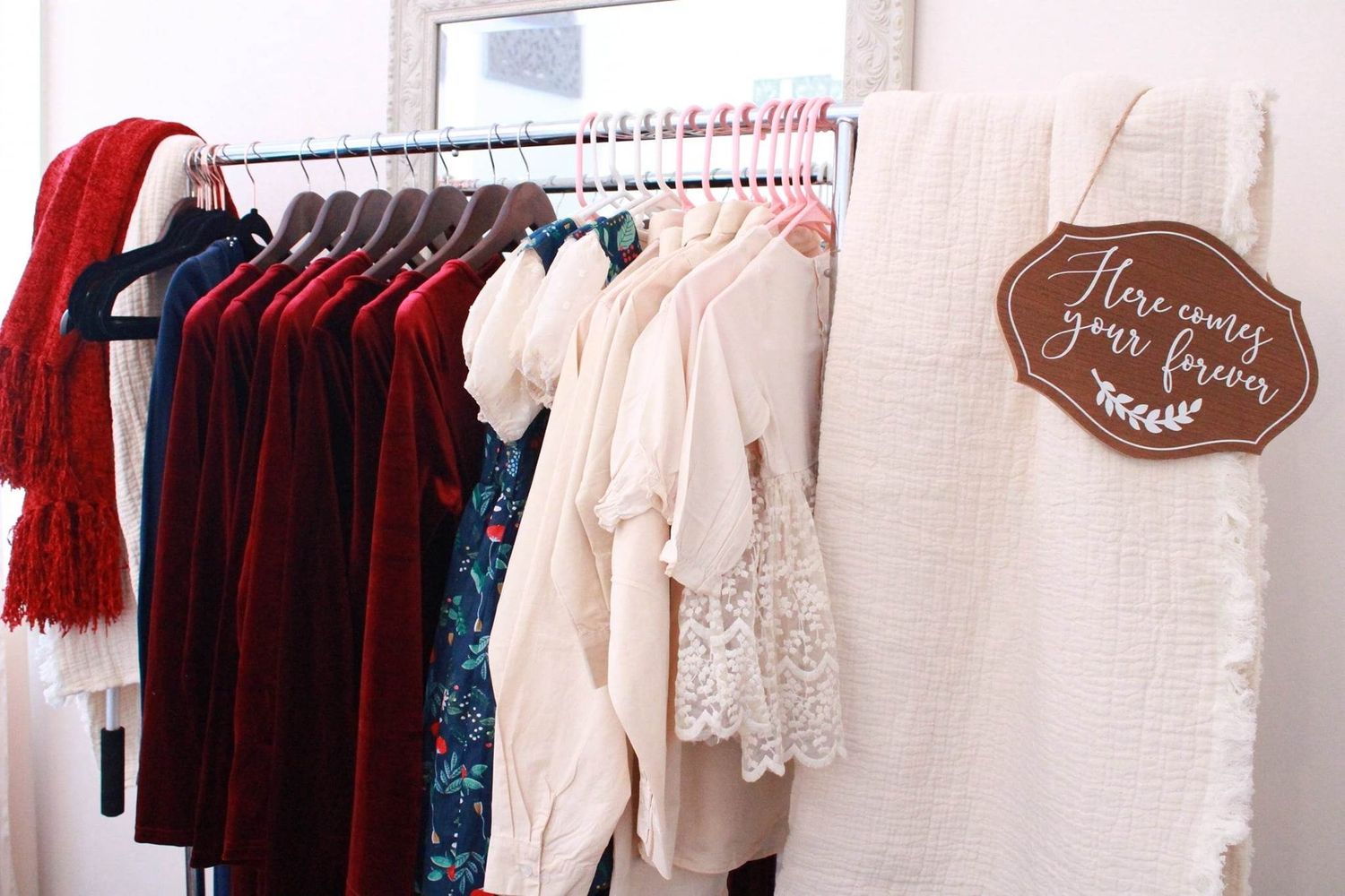 Wedding attire displayed on clothing rack with burgundy and cream colored dresses and accessories.