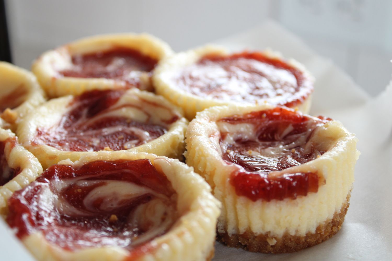 Mini raspberry swirl cheesecakes with graham cracker crusts.