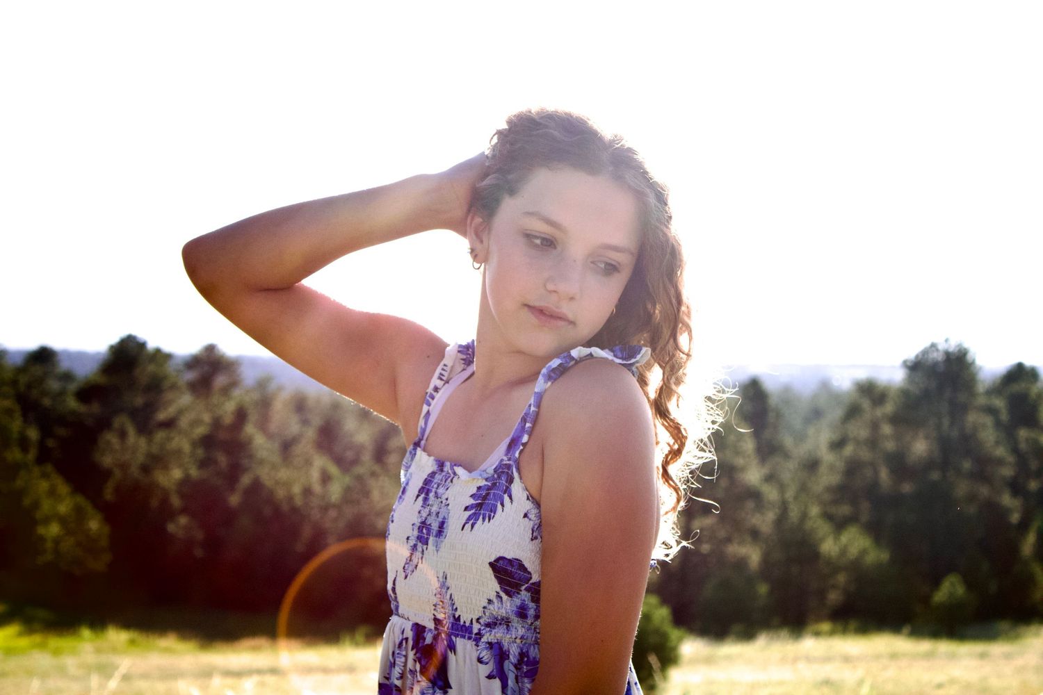 A person wearing a floral dress poses in a sunlit meadow during golden hour.