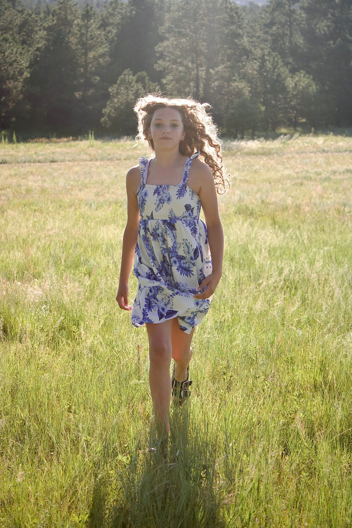 A person wearing a floral dress runs playfully through a sun-lit meadow of tall grass on a summer day.