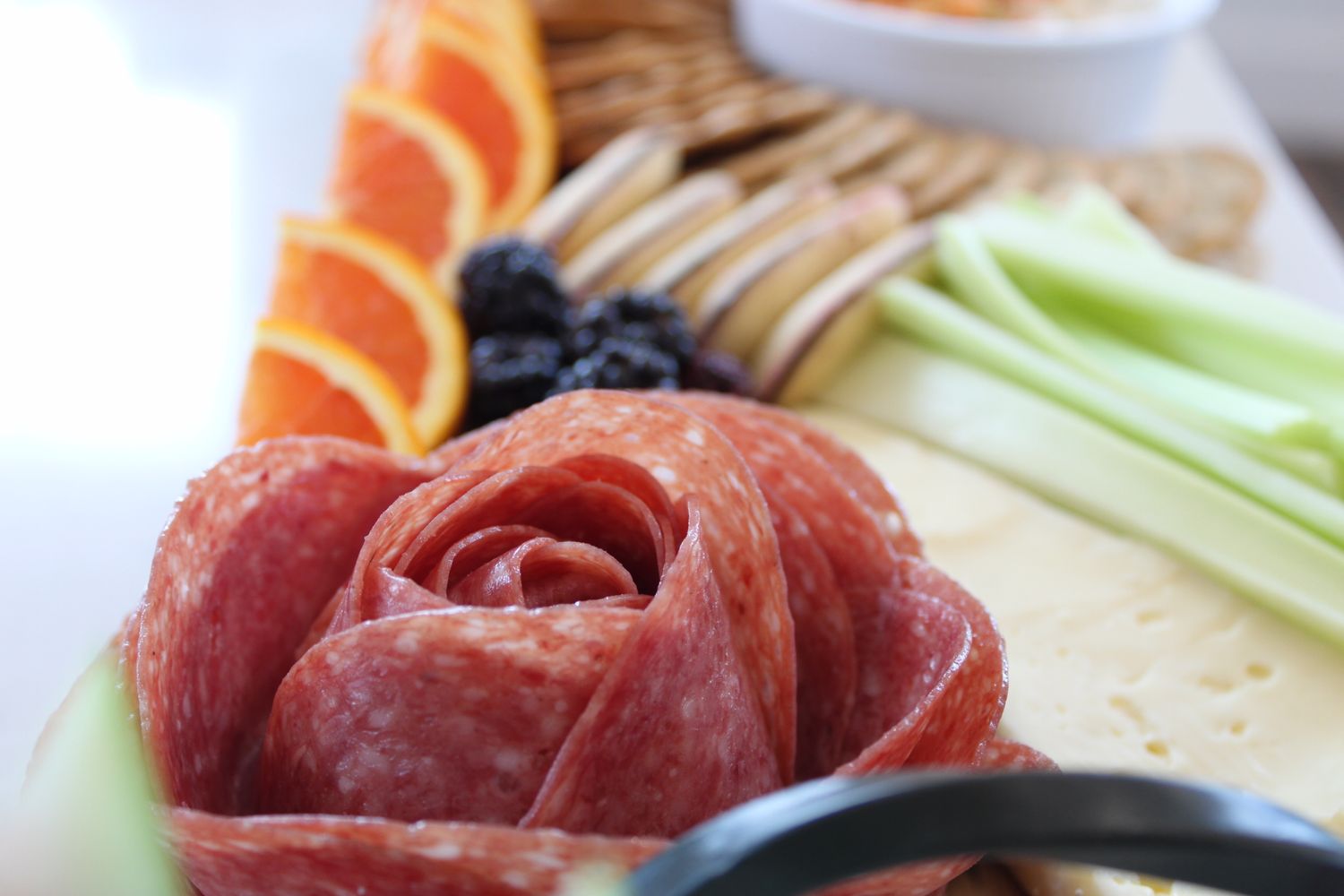 Charcuterie board with rolled salami, orange slices, and celery sticks.