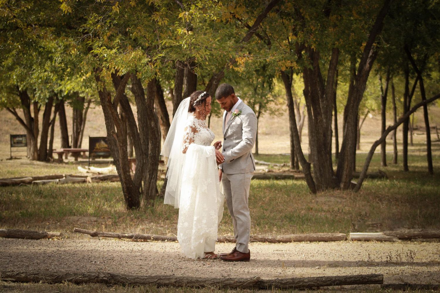 Wedding couple strolls through wooded area in elegant attire.