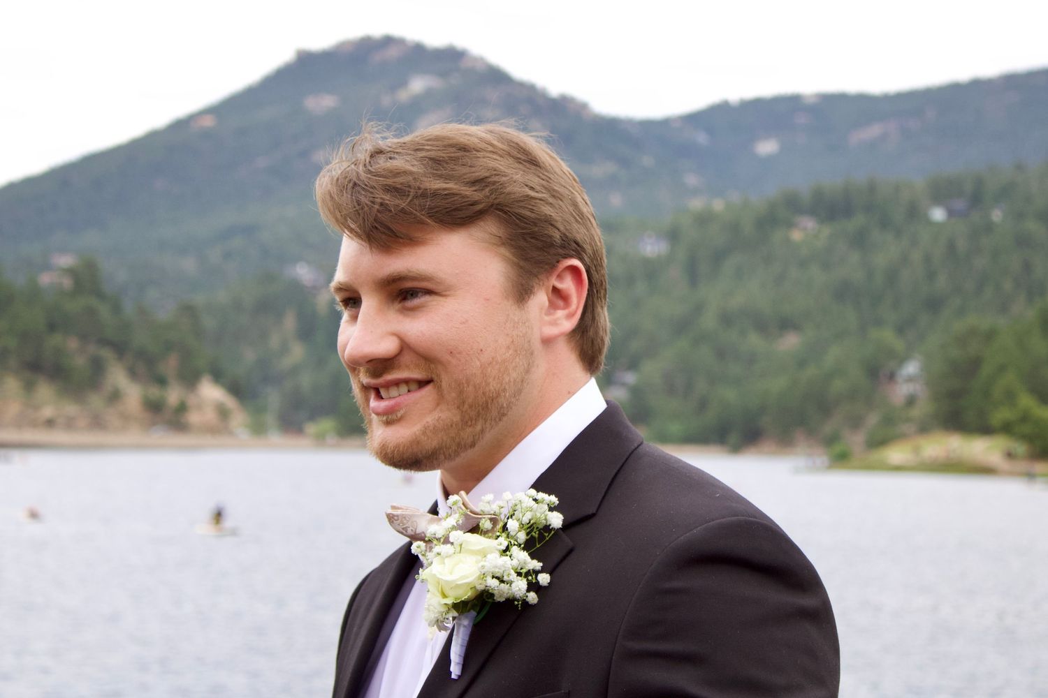 Groomsmen in black suits pose together outdoors with a mountain landscape in the background.