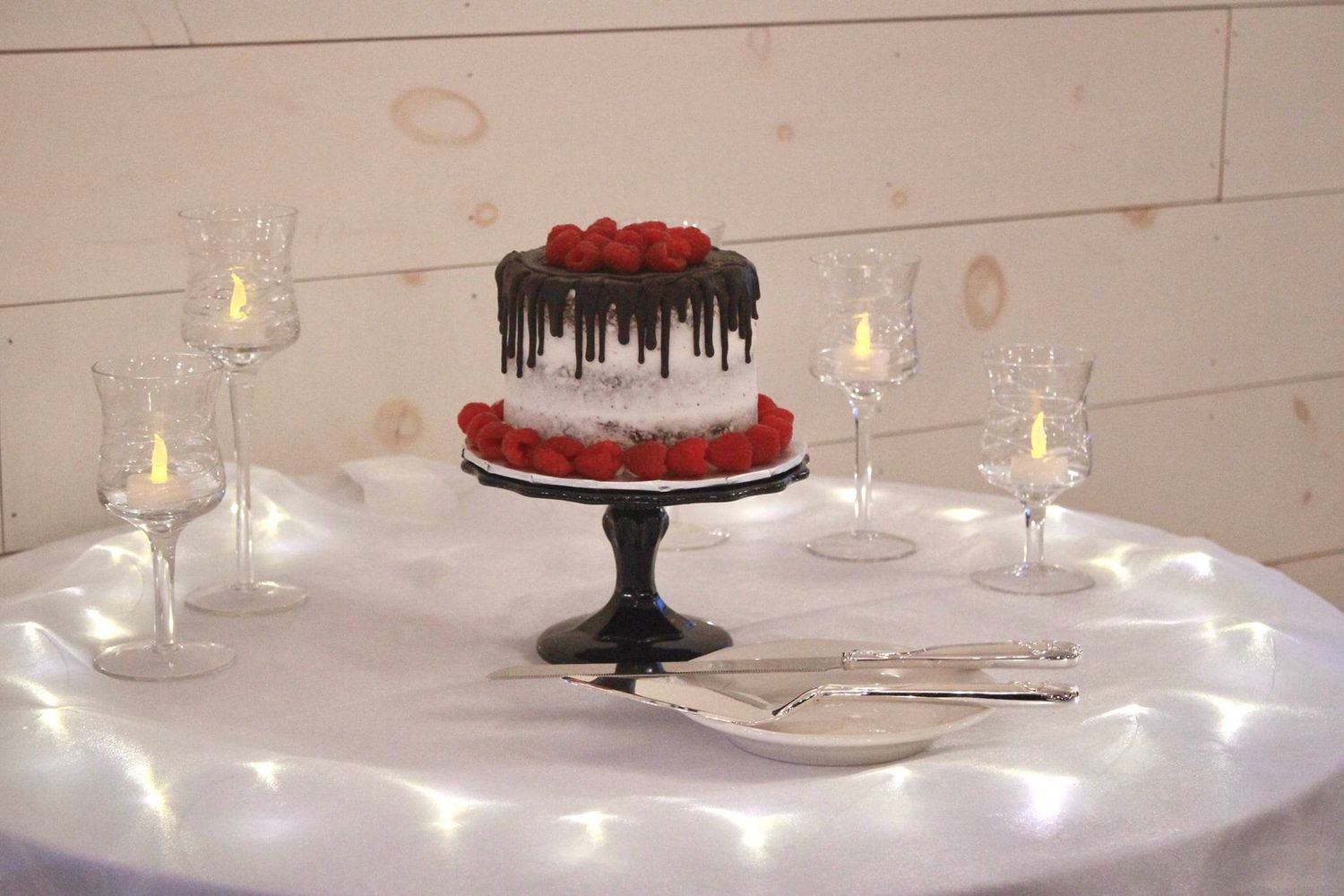 Red and white wedding cake with drip decoration displayed on black stand with candle lighting.