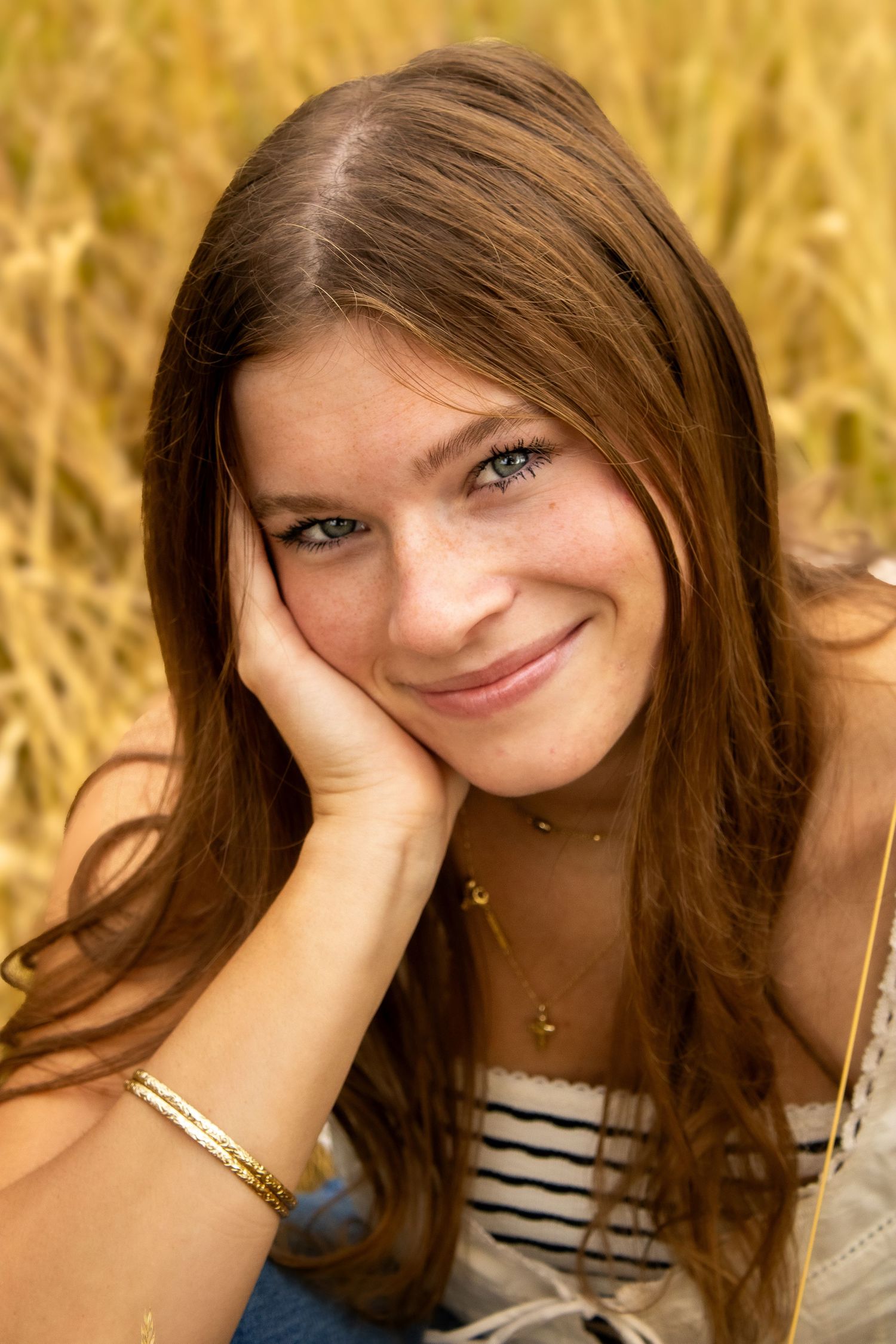 Portrait of a smiling young woman wearing a striped top against a golden wheat field background.