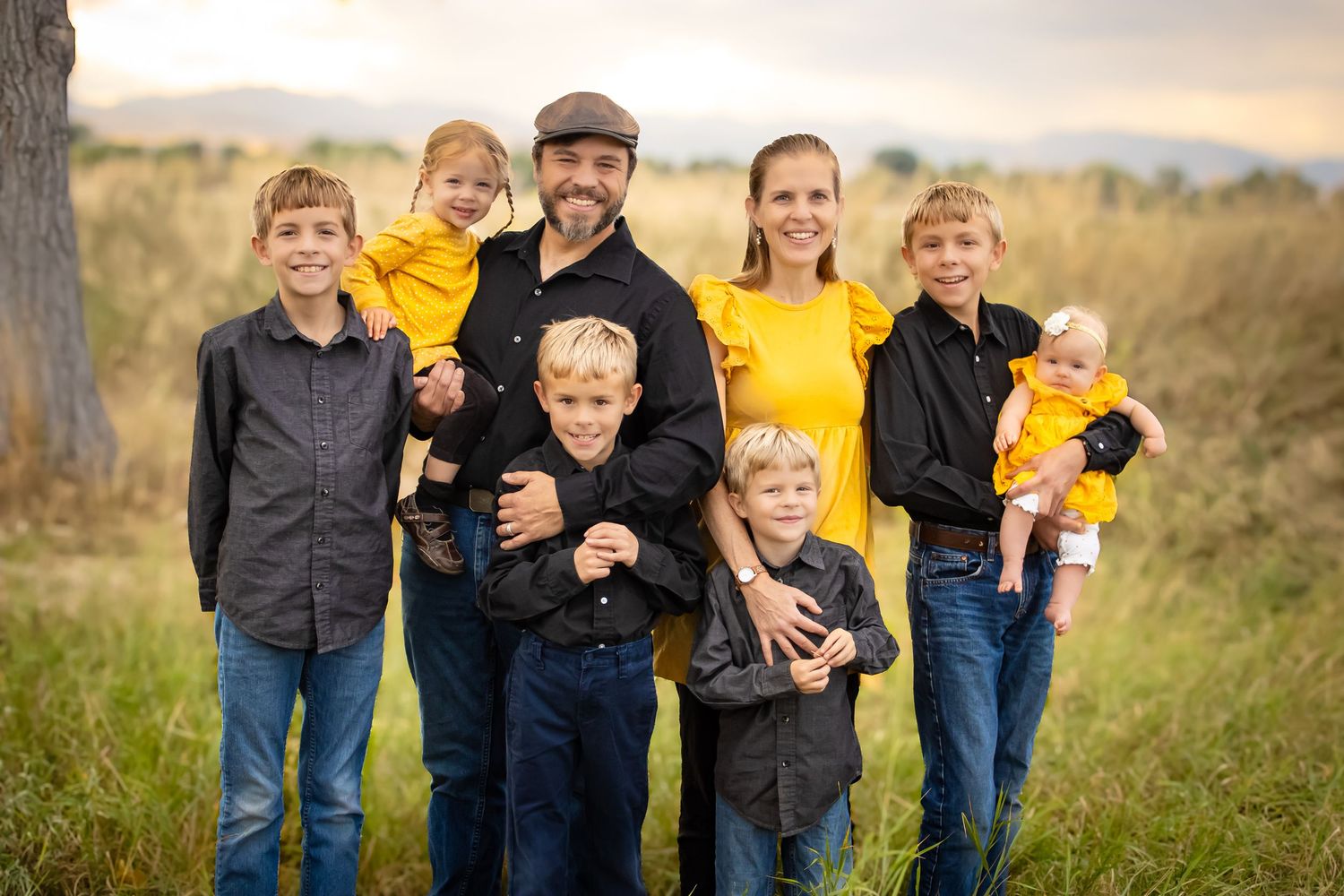 A family wearing coordinated navy and yellow outfits poses together in a grassy field during golden hour.