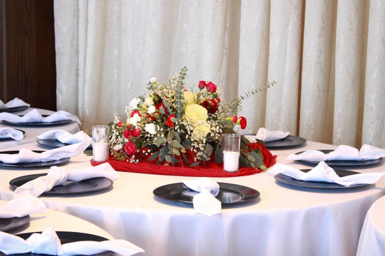 Elegant table setting with red and yellow floral centerpiece on white tablecloth with navy napkins.