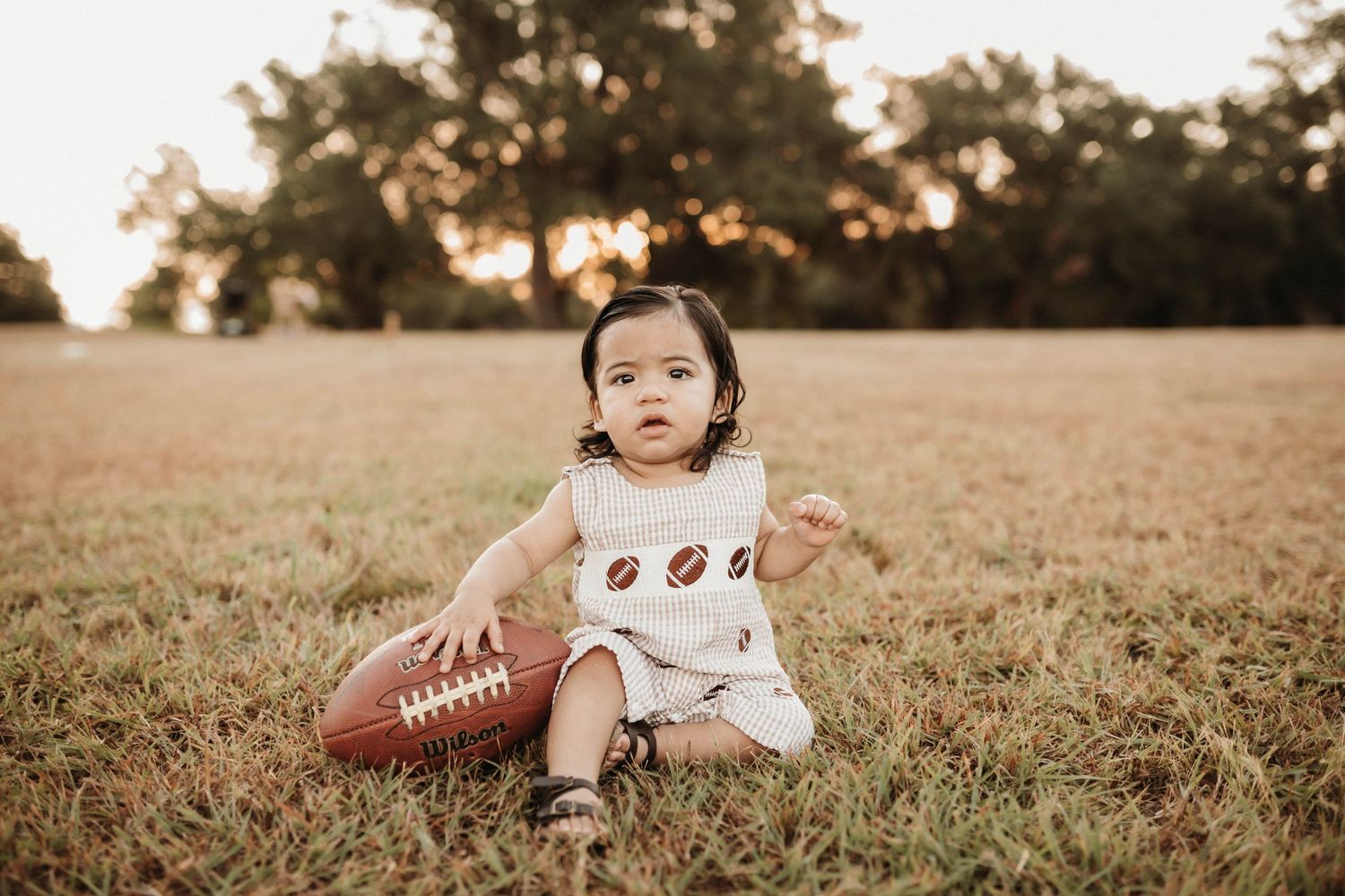 A football rests in a grassy field during golden hour sunset lighting.