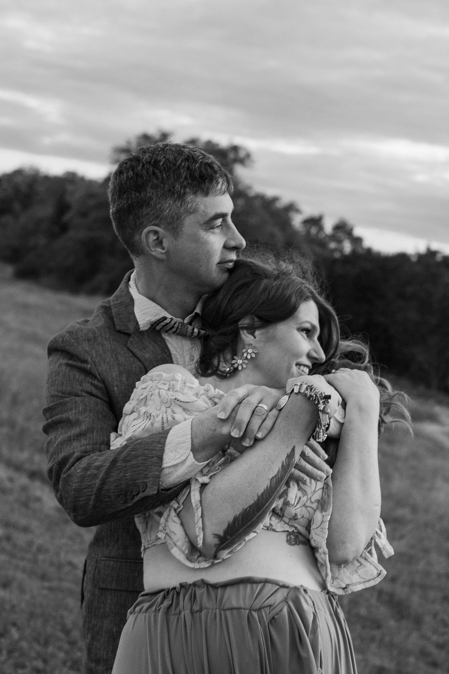 Intimate black and white portrait of couple embracing on hillside.
