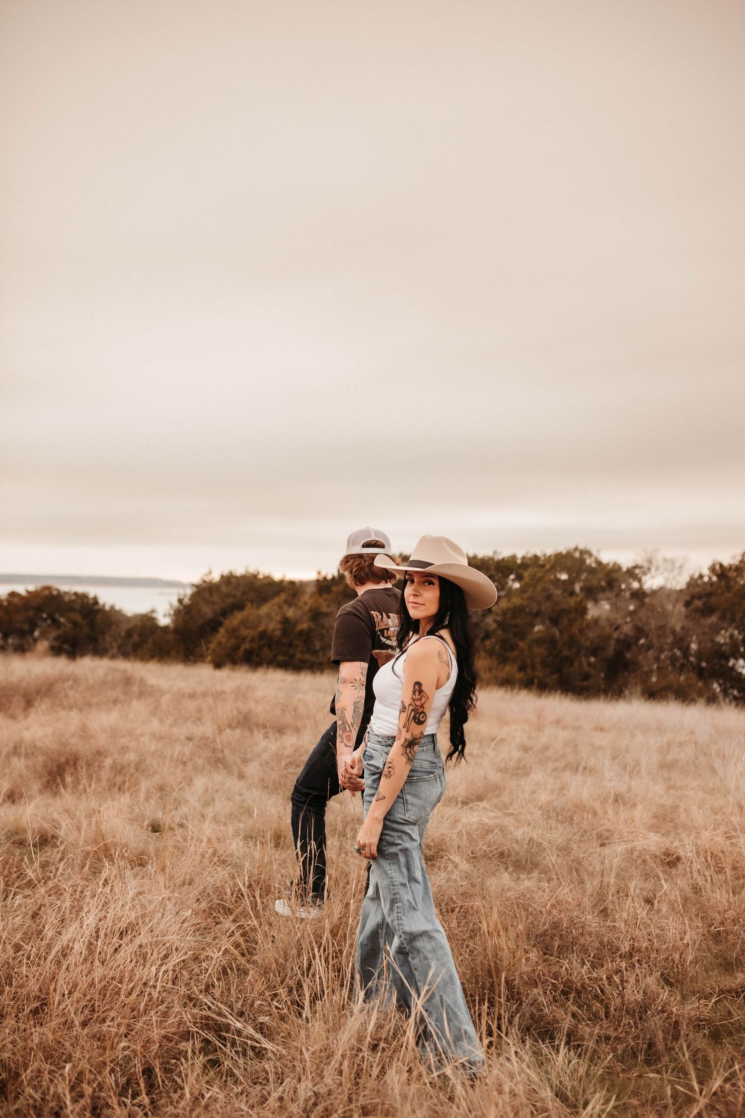 A couple in western attire standing together in a sun-drenched autumn field.