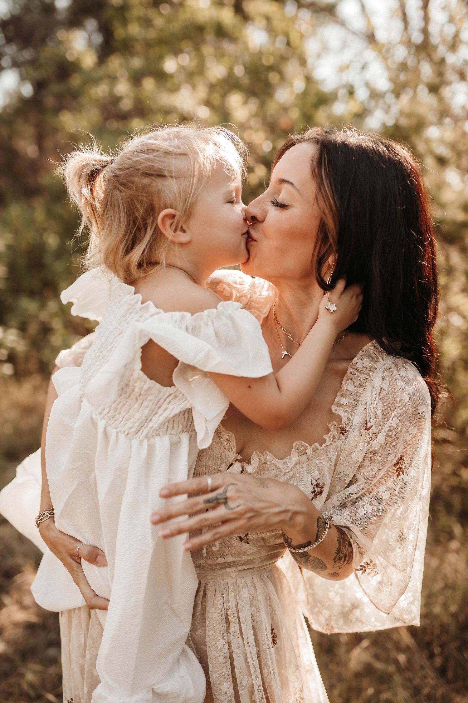 A tender moment between a parent and child wearing white dresses in warm sunlit outdoor setting.
