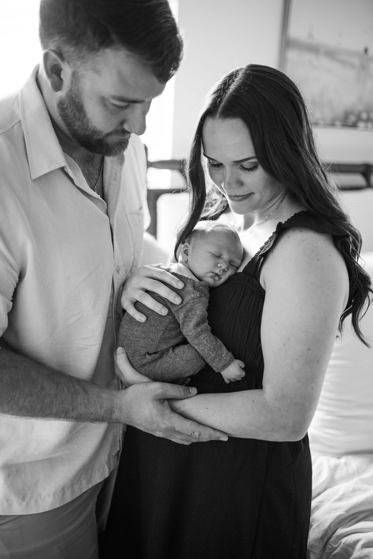 Black and white photo series showing tender moments between parents and their newborn baby in intimate home setting.