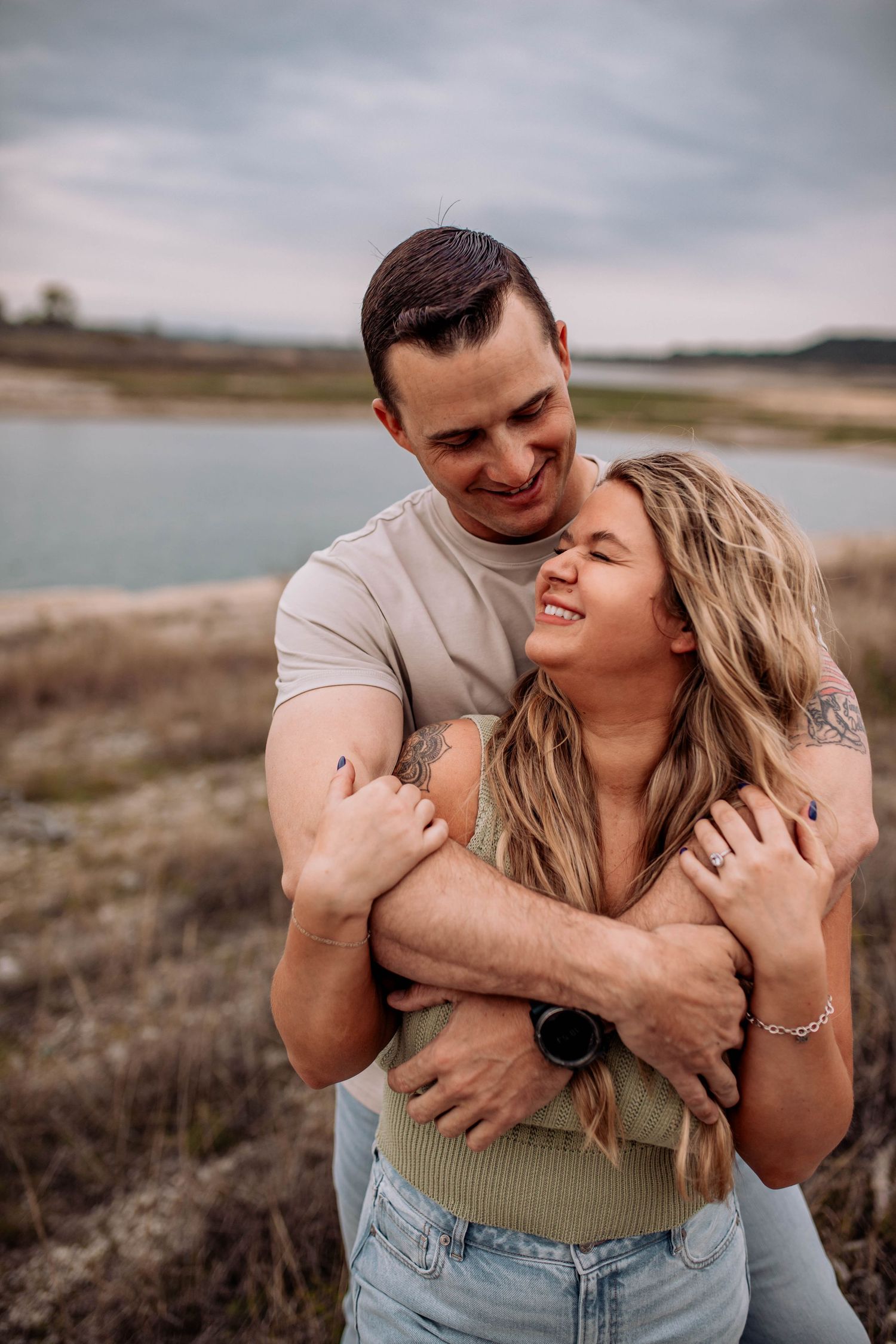 A couple shares an intimate embrace against a cloudy lakeside backdrop.